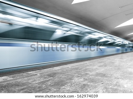 Perspective and diminishing wide angle view of modern light blue illuminated and spacious public metro marble abstract station, fast blurred trail of quick urban train in vanishing traffic motion way