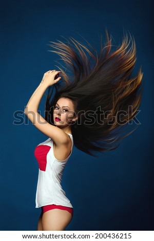 Portrait of beauty attractive fashion slim healthy young woman with fluttering hair and perfect training sexy tanned skin sport body in an ideal white and red lingerie isolated on dark blue background