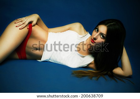 Portrait of beauty attractive fashion slim healthy young woman lying with perfect training sexy tanned skin sport body in an ideal white and red lingerie on dark blue background
