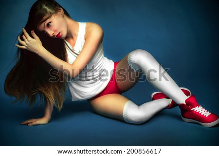 Portrait of beauty attractive fashion slim healthy young woman sitting with perfect training sexy tanned skin sport body in an ideal white and red lingerie, sporty shoes on dark blue background