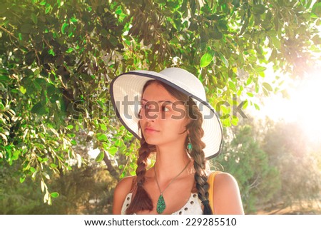 Summer closeup portrait of pretty tender beautiful young female face with clear skin and delicate complexion in the autumn evening sunshine in nature with big white hat and cute dreadlocks