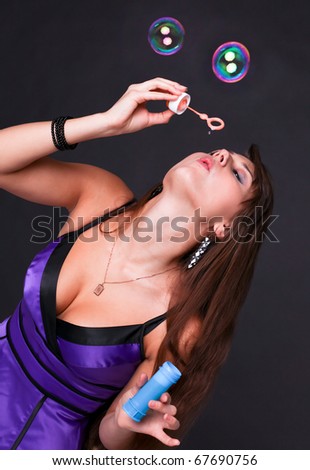 Portrait of funny lovely teenage girl inflating colorful soap bubbles, studio shot