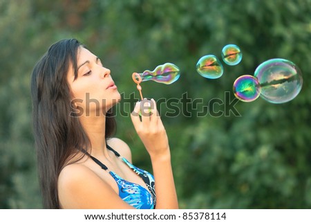 beautiful young girl inflating colorful soap bubbles in nature