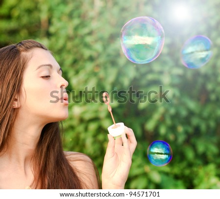 Beautiful young woman inflating soap-bubbles in spring