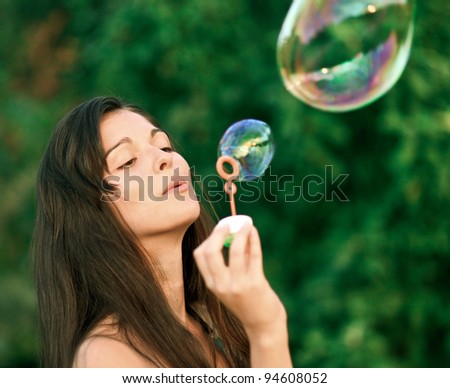 Beautiful young woman inflating colorful soap bubbles in pure nature