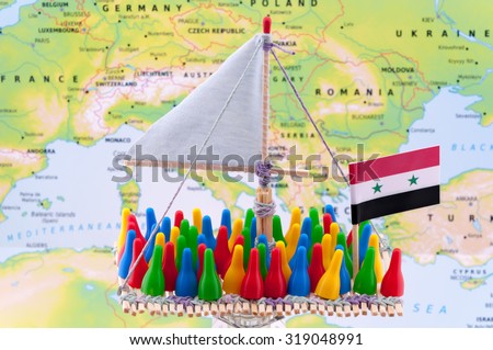 Wooden raft with sail and flag of Syria embarked with big crowd of colorful game pieces that supposed to be looking similar to refugees escaping from Syria. Map of mediterranean sea in the background.
