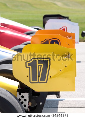 Racing cars lined up in the pit area.  Rear wings.