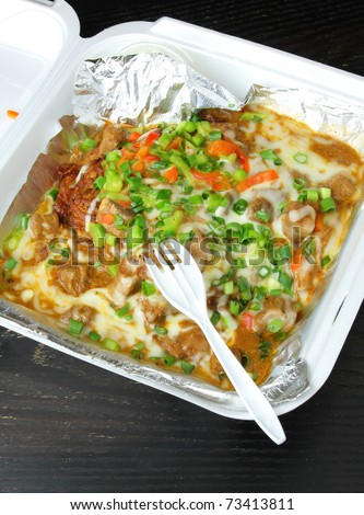 Tasty, colorful take-out food in a box.  Potato pancake with meat and vegetables covered in cheese and sauce