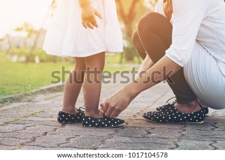 Mother tying shoe  little girl in the park selective focus.