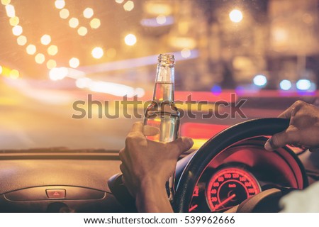 Drunk young man driving a car with a bottle of beer. Don\'t drink and drive concept. Driving under the influence. DUI, Driving while intoxicated.