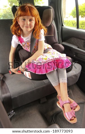 young girl clicking shut her seat belt in a child restraint seat in the back of a car