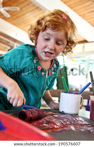 little red headed girl painting at her preschool kindergarten class