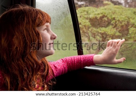 little red haired girl looking out car window onto natural scenery on a rainy, winter day in New Zealand