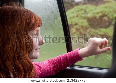 little red haired girl looking out car window onto natural scenery on a rainy, winter day in New Zealand