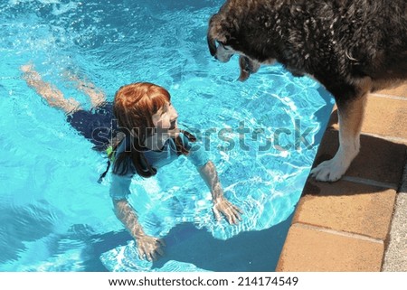 little red haired girl in swimming pool with her dog watching over her from the edge