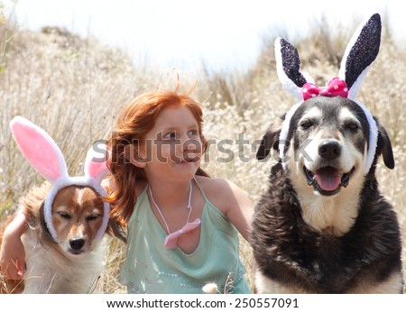 little red haired girl dressing her pet dogs up as easter bunnies for an easter egg hunt outdoors