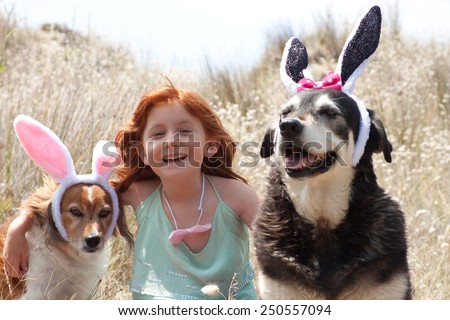little red haired girl dressing her pet dogs up as easter bunnies for an easter egg hunt outdoors