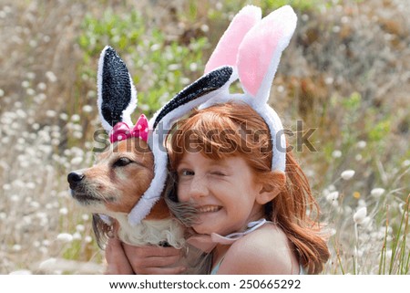little red haired girl with her pet dog dressed up as Easter bunny on an easter egg hunt in meadow of bunnies tail grass