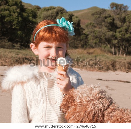 curly haired dog watching young red haired girl eating waffle cone ice cream at a beach in New Zealand
