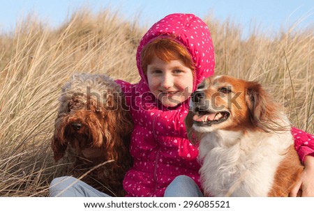 red haired girl in winter jacket hugging red haired collie type dog on a cold winter's day in grassy sand dunes at a beach in Gisborne, New Zealand