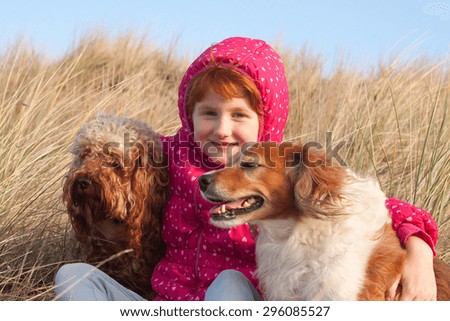 red haired girl in winter jacket hugging red haired collie type dog on a cold winter\'s day in grassy sand dunes at a beach in Gisborne, New Zealand