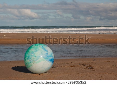 concept image for global environmental issue using inflatable rubber ball with earth like markings against an ocean beach background traditional landscape format