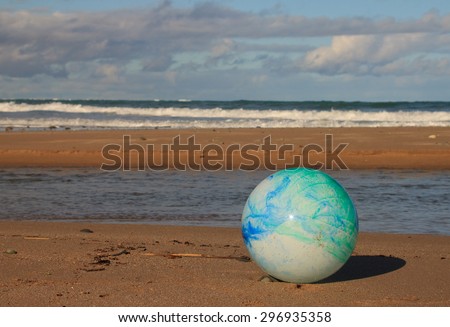concept image for global environmental issue using inflatable rubber ball with earth like markings against an ocean beach background traditional landscape format
