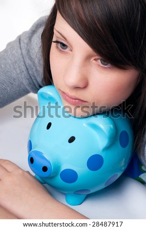 young girl with far away look in eyes and resting chin on blue spotted piggy bank. Hands crossed isolated on white background