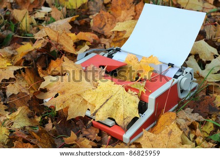 Vintage manual shabby typewriter, blank sheet of paper and fallen maple leaves in the fall