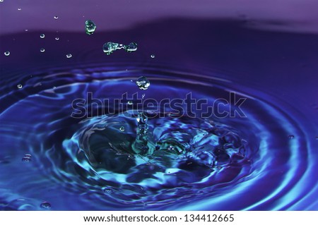 Colored water droplets collisions macro..  Closeup of multiple green water droplets gall into blue and purple water.