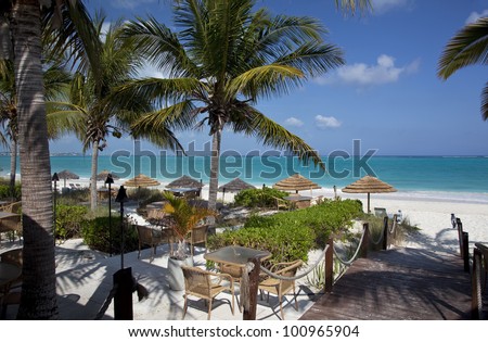 A restaurant on Grace Bay Beach, Providenciales, Turks and Caicos Islands.  Tiki umbrellas and palm trees accent the blue-green water and white-sand beach.