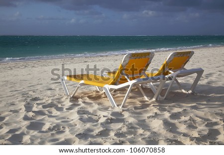 Two unoccupied yellow lounge chairs at the end of the day at Grace Bay Beach, Providenciales, Turks and Caicos Islands.  The beach is empty.  White sand, blue-green water, and a clouded blue sky.
