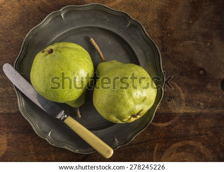 Fresh green pears on a pewter plate with a vintage knife, placed on a distressed wood table, photographed from above. Close up.