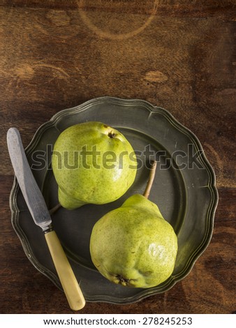 Fresh green pears on a pewter plate with a vintage knife, placed on a distressed wood table, photographed from above.