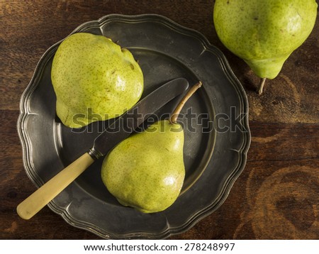 Fresh green pears on a distressed wooden table. One of the pears has been sliced and placed on a pewter plate.