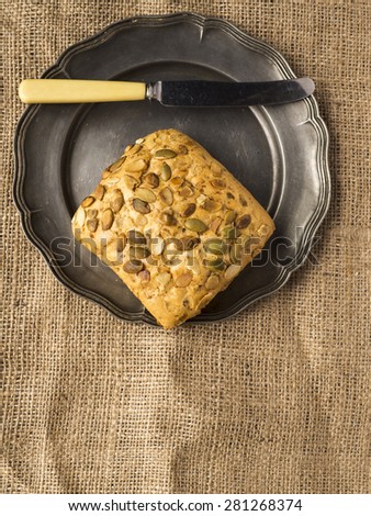 A fresh pumpkin seed roll on a pewer plate with a knife. They are resting on a rustic sacking cloth
