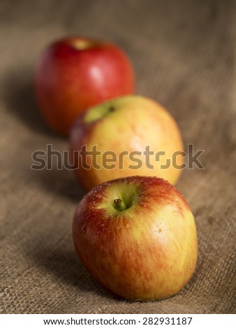 Three apples covered in water droplets sitting on a sackcloth background.  The depth of field is limited so that only the front apple is in sharp focus.