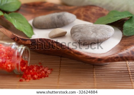 Massage stones on sand in a bowl and red bath salt