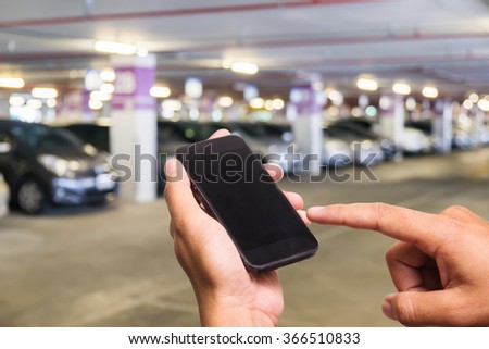 Hand of a man holding a smartphone and touching the screen.Parking lot