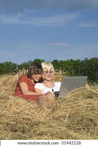 Two Young girl work with laptop in a stack of hay