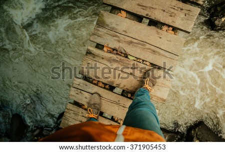 Man\'s legs on an old wooden bridge through the river
