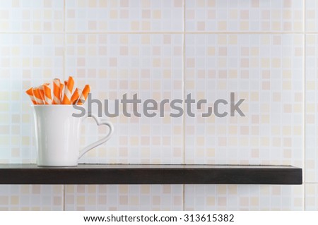 A cup of orange wafer rolls on shelf.