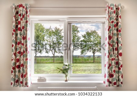 Window with a view onto fields and trees in a rural setting. Curtains and a bright summers day make this a beautiful scene and a place anyone would love to live