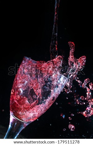 Wine pouring and spilling into a glass frozen in time, on a black background