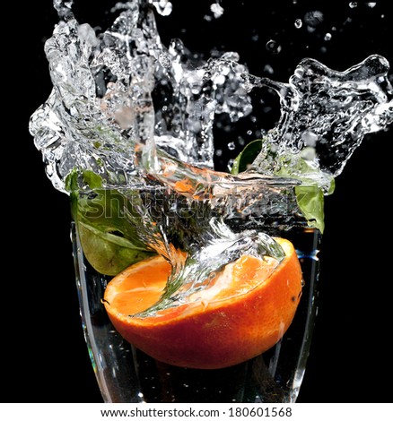Orange dropped into a glass of water with big splash frozen in time, on a black background