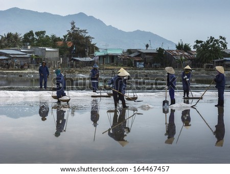 COASTLINE, SOUTH VIETNAM - CIRCA MARCH 2012: A crew of several people harvest salt by raking, scooping and carrying it away while standing in the shallow pool.