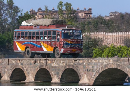 ORCHHA, INDIA - CIRCA FEBRUARY 2011: Public transport bus traverses bridge over Betwa River with Raja Palace in background.