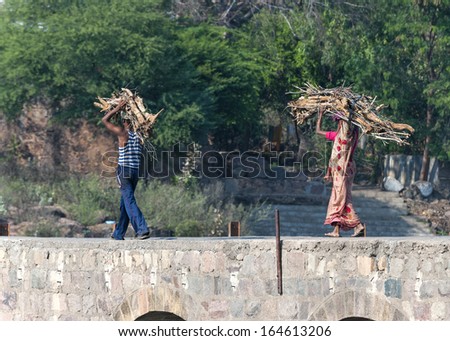 ORCHHA, INDIA - FEBRUARY 2011 - Man and woman, in sari, carry firewood on head over bridge.