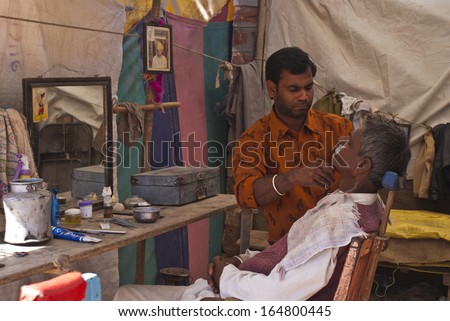 NAGAUR, INDIA - CIRCA FEBRUARY 2011: Typical small India barber shop in tent along the street. Focus on the barber and his client still with white foam on his face.