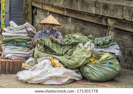 HANOI, VIETNAM - CIRCA MARCH 2012: Woman repairs old plastic bags in the street of Hanoi. Recycling and reusing green and white garbage sacks.